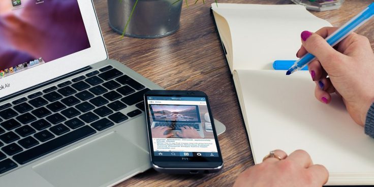 tavolo con pc portatile, smartphone e mano che scrive